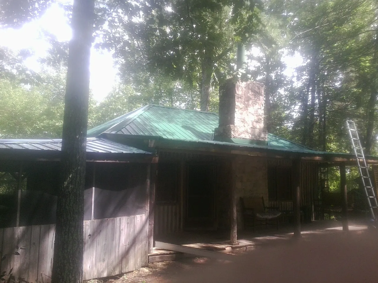 Green metal roof and stone chimney above a log cabin porch in Johnstown
